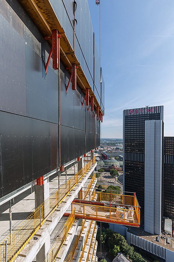 Die Einhausung mit der RCS Kletterschutzwand umschloss die obersten Rohbaugeschosse und sicherte das Personal vor Absturz und vor starkem Wind in großer Höhe. RCS Ausfahrbühnen und der PROKIT Seitenschutz ergänzten die PERI Gesamtlösung sinnvoll.