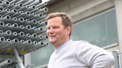 Walter Buchsteiner steht vor den Systembauteilen des PERI UP Gerüstbaukastens.