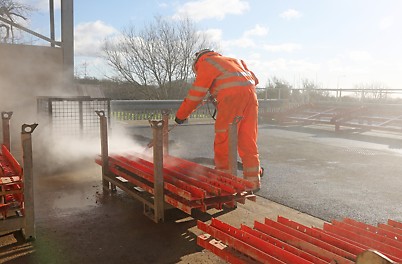 Our teams can support you with cleaning and repair services. A person power washes formwork to remove debris.