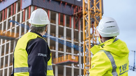 Zwei Männer stehen auf der Baustelle und zeigen in Richtung eines Gebäudes