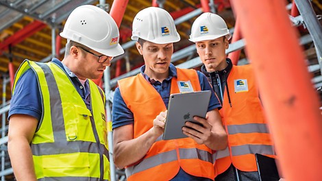 Drei Männer auf der Baustelle, schauen auf ein Tablet