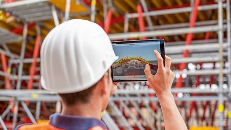 Das Bild zeigt einen Mann, der ein Tablet in der Hand hält, welches die digitalisierte Version der Baustelle im Hintergrund zeigt.