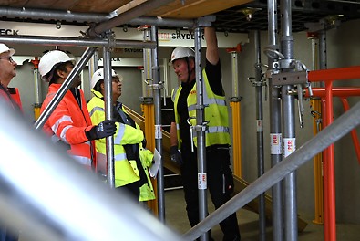 Delegates in hard hats and high-vs jackets watch as a trainer from PERI UK shows them how SKYDECK, a PERI product works.