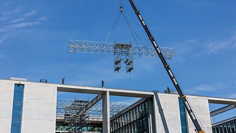 Nach der Fertigmontage am Boden lassen sich die 24 m langen und 2,50 m breiten PERI UP Gerüsteinheiten mit dem Mobilkran auf das Dach einheben und anschließend von Hand nach innen hin verfahren.