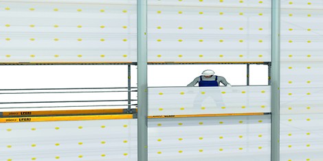 A worker on a scaffolding system that is up a building. They are holding a panel.