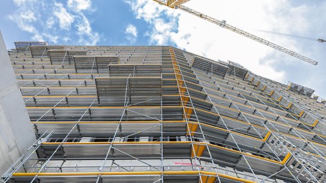 Versetzt angeordnet In das PERI UP Fassadengerüst integrierte Absetzbühnen kragen jeweils 1,50 m nach außen aus und dienen zur Andienung, Lagerung und Vormontage der Fassadenelemente.