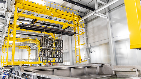 The image shows the new coating factory for PERI. A piece of equipment is on a conveyor belt being prepared to be dipped, and coated.