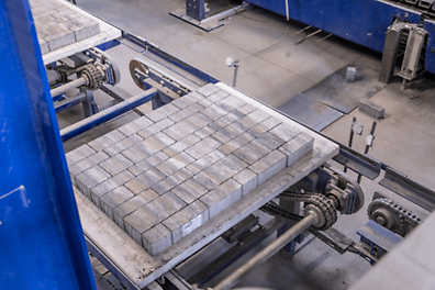 A factory shows grey PERI Pave blocks on a conveyor belt.