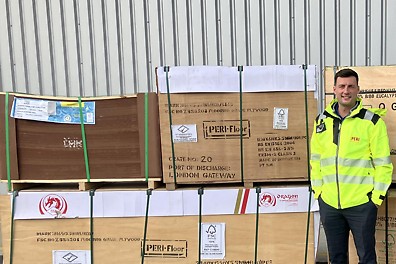 A man in high vis stood in front of a pallet of plywood panels.