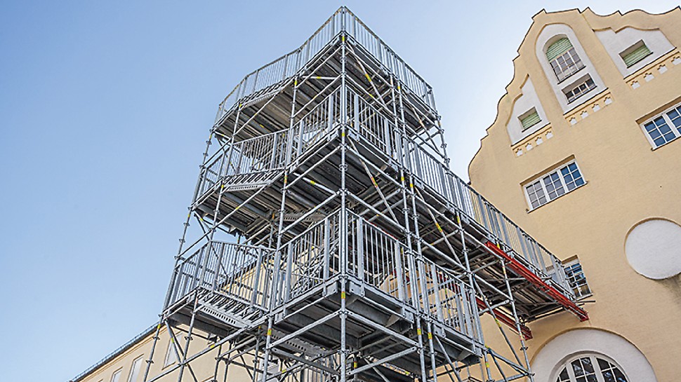 Pendant les travaux de rénovation, cette tour d'escalier de 14 m de haut sert d'issue de secours. Les composants du système VARIOKIT facilitent le transfert vers le bâtiment.