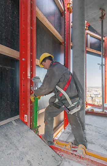 A worker, who positions the climbing rail and the climbing shoe on the RCS protection panel unit with a mobile hydraulic cylinder.