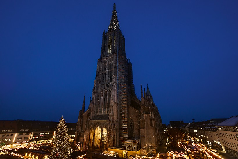 Ulmer Münster und der am Fuße der Kirche leuchtende Ulmer Weihnachtsmarkt bei Nacht. 
