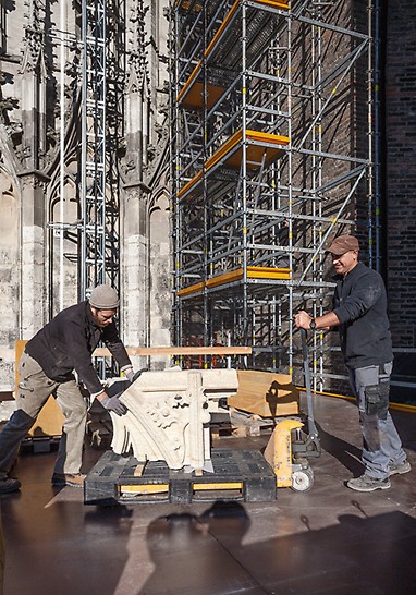 Zwei Männer transportieren auf der PERI UP Plattform einen schweren Stein mit Ornamenten, welcher im Bauwerk des Ulmer Münsters ausgetauscht werden soll.