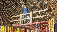Pracovník stojící na bednicím vozíku provádí instalační práce na klenutém stropu.