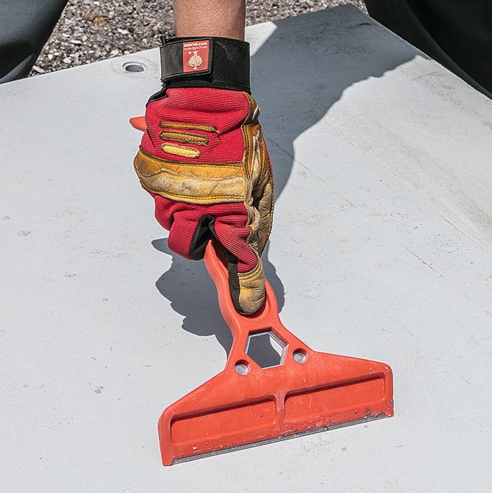 Removing concrete residue from a formwork panel with a scraper