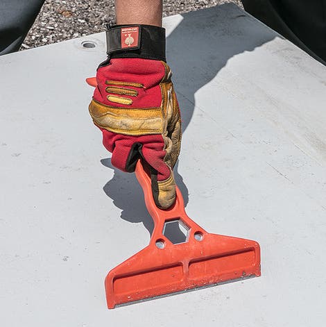Removing concrete residue from a formwork panel with a scraper