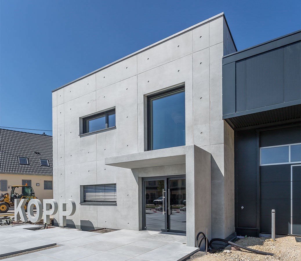 Das moderne, zweigeschossige Bürogebäude besticht durch seine sehenswerte Sichtbetonfassade mit einem klar gegliederten Fugen und Ankerraster.