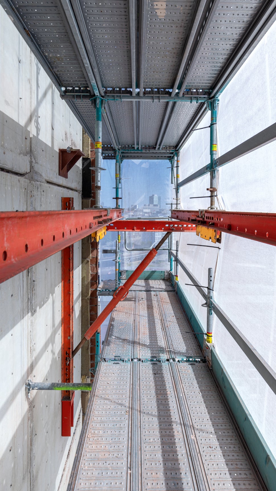 Die gerüsttechnische Herausforderung versteckt sich hinter den Staubschutznetzen: In regelmäßigen Abständen lagert das PERI UP Gerüst auf VARIOKIT Konsollagen, da die Lasteinleitung auf das Dach des Sockelbauwerks aus bauwerksstatischen Gründen eingeschränkt war.