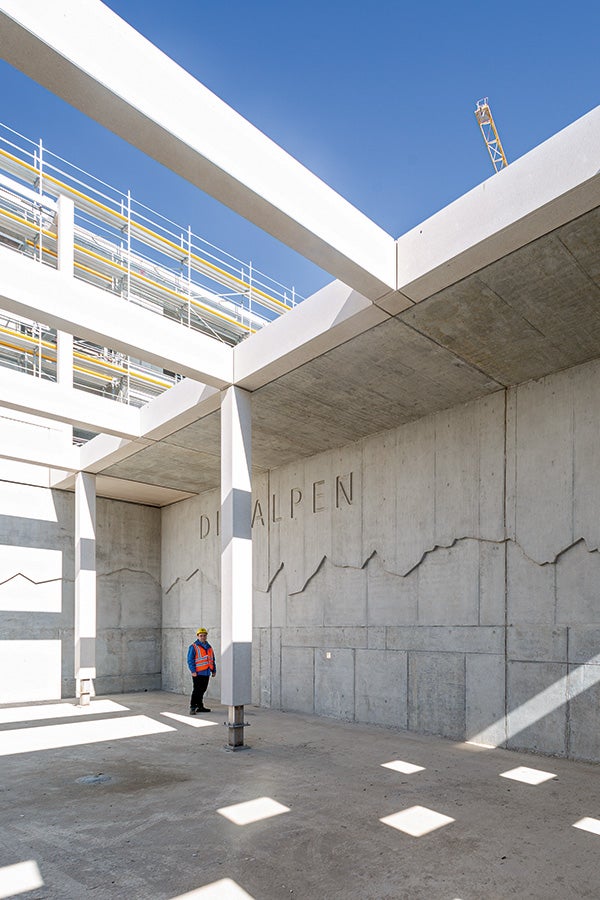 Velkoplošný betonový obraz panorama Alp ve dvoře základní školy s přesně zobrazenými vrcholky hor podle vyfrézované bednicí desky připravené v montážní dílně PERI. 