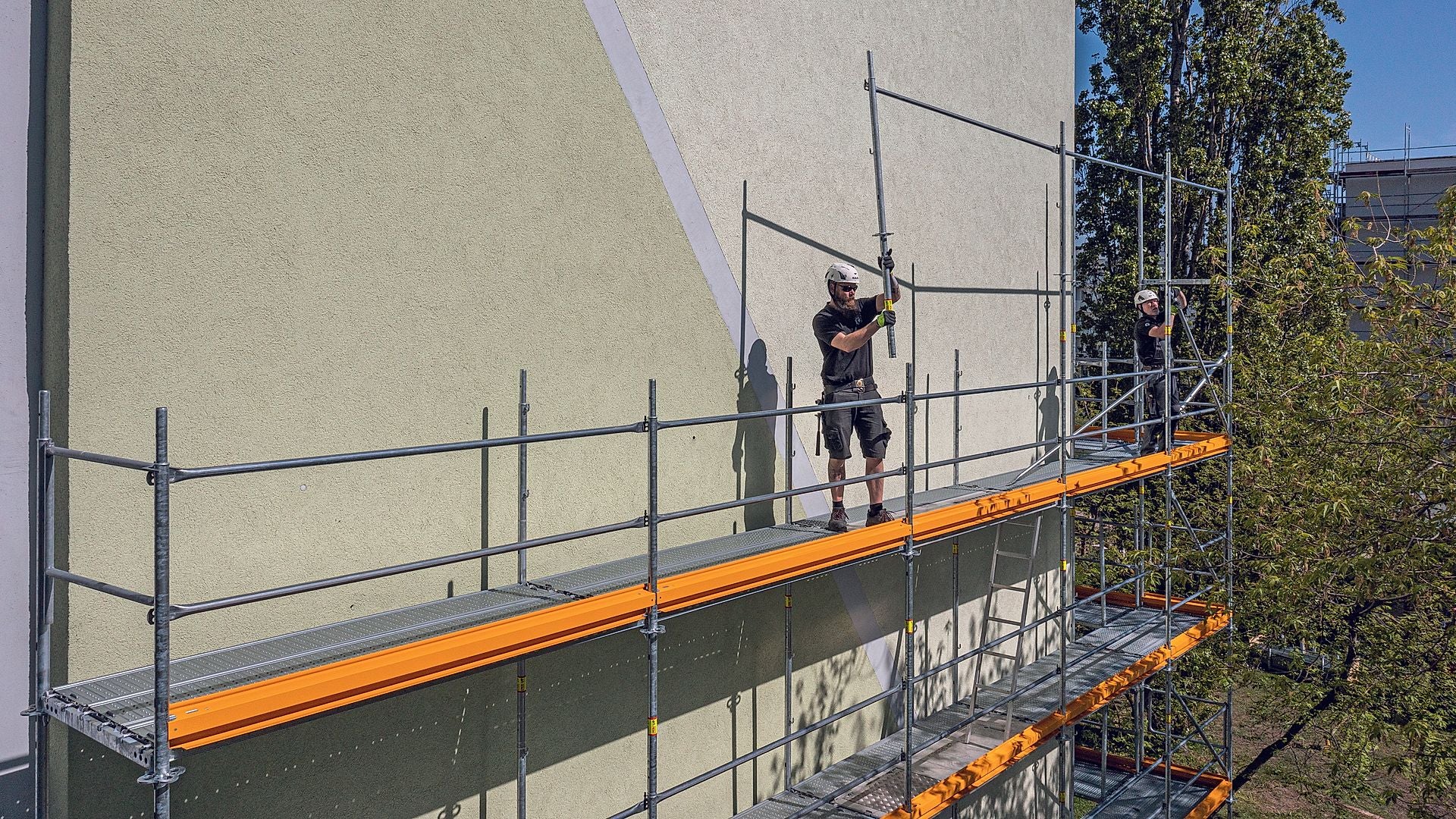 Das Geländer für die nächste Ebene wird mit dem Easy Stiel von der unteren Gerüstlage aus montiert. So entsteht bereits beim Aufbau eine systemintegrierte Absturzsicherung ohne zusätzliche Bauteile.