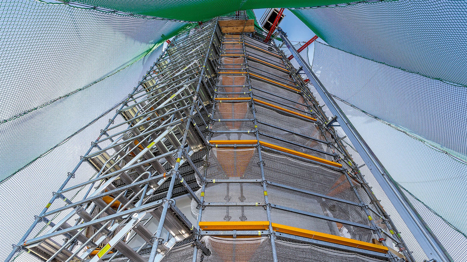 Circular scaffolding and a connection actuated by gravity at the tower top between 192 m and 243 m with ledgers of the PERI UP Flex modular scaffolding system. Also the setting up of the guardrail takes place without a time-consuming tube-and-coupler system.<br/>