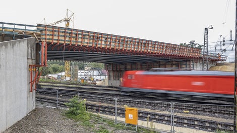 Die VARIOKIT Gesimskappenschalung setzt sich aus Bühneneinheit und Schalungseinheit zusammen. Beides hängt an der Brücke, wodurch der unten laufende Verkehr nicht gestört wird, während den Sanierungsarbeiten voranschreiten.