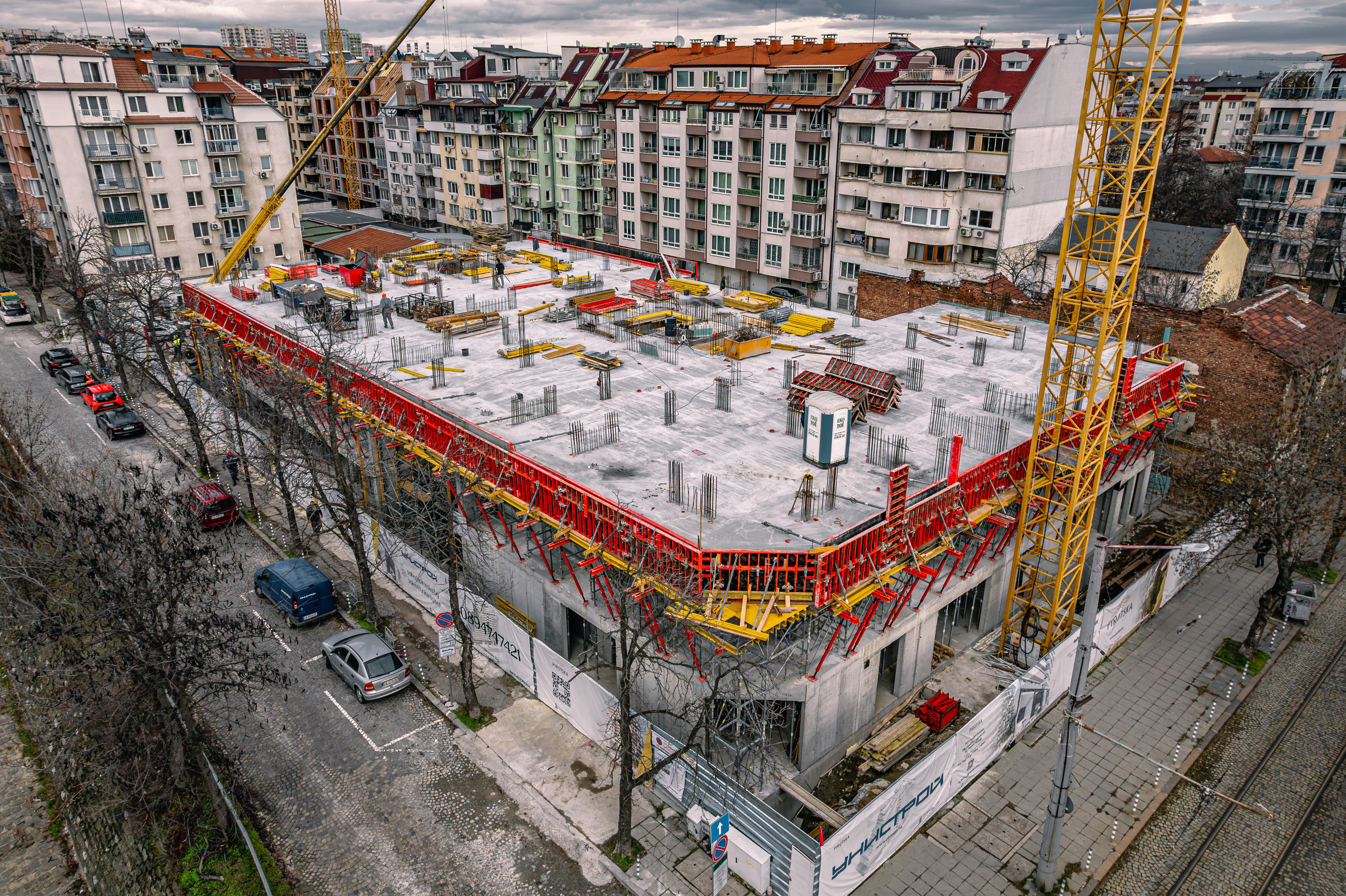 Общ въздушен кадър на сградата между ул. „Пиротска“ и бул. „инж. Иван Иванов“, показващ поетапното изпълнение в гъсто застроен район.