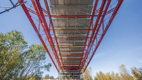 Mit bis zu 26,50 m Spannweite überspannen VARIOKIT Fachwerkträger das Gelände zwischen den Stahlstützen der Bandbrücke und tragen das für die Sanierung notwendige PERI UP Arbeits- und Schutzgerüst.