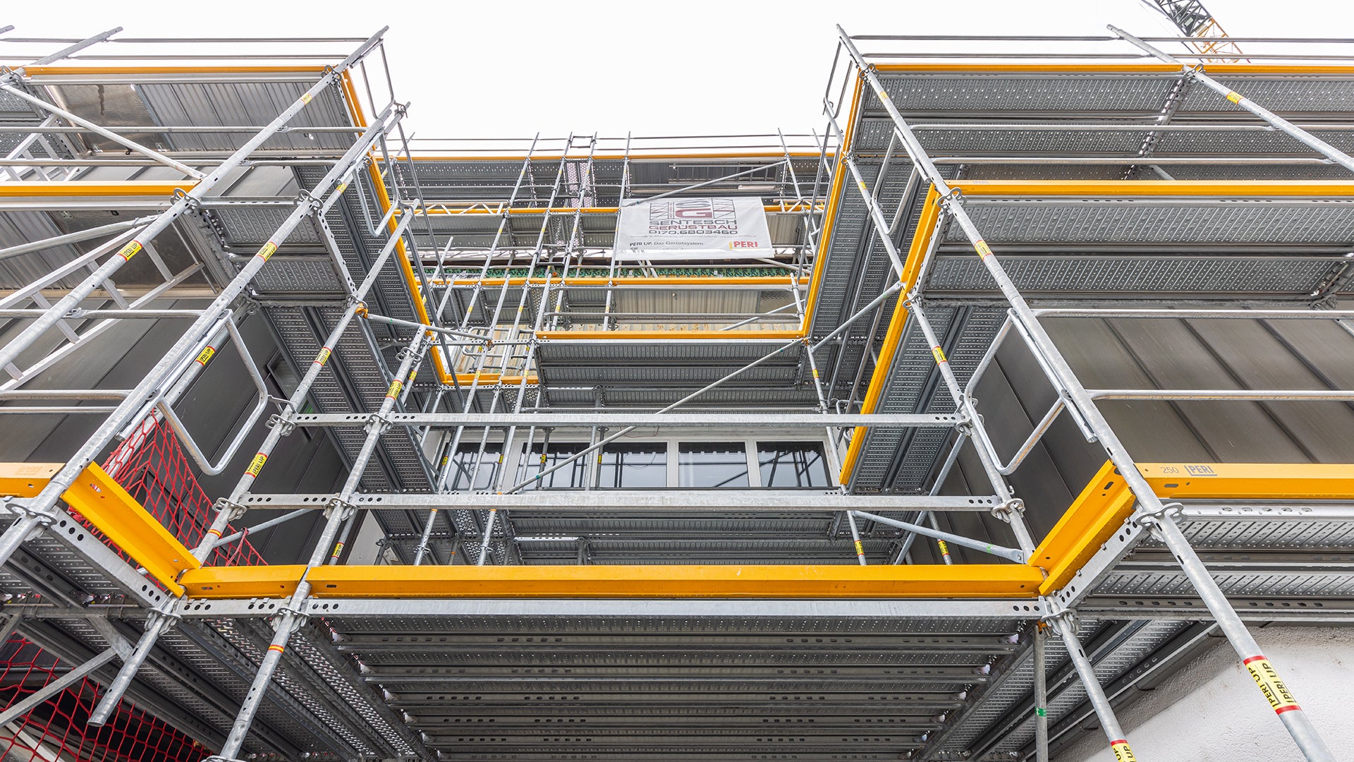 Der Gerüstknoten am Easy-Stiel ermöglichte außen- und innenseitige Anbauten und den nahtlosen Übergang von Easy- auf Flex-Bauteile, beispielsweise für die Schutzdachausbildung im Zugangsbereich zur Halle und als vorgelagerte Absetzbühne.