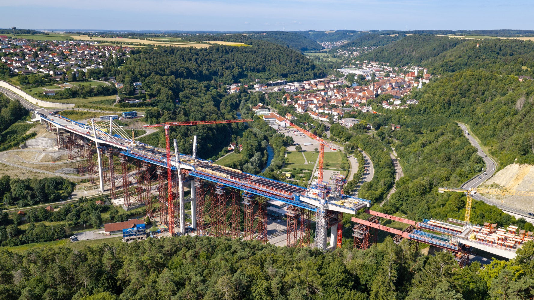 Im Sommer 2026 nimmt die Neckarbrücke Horb zunehmend ihre endgültige Form an: Große Teile des Überbaus sind bereits fertiggestellt, auch die ersten Pylone und Schrägseile prägen inzwischen das Erscheinungsbild. Die Fertigstellung der Brücke ist für 2028 vorgesehen.